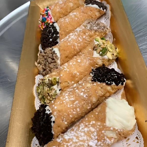 A golden tray filled with various cannoli, some topped with sprinkles, nuts, and chocolate.