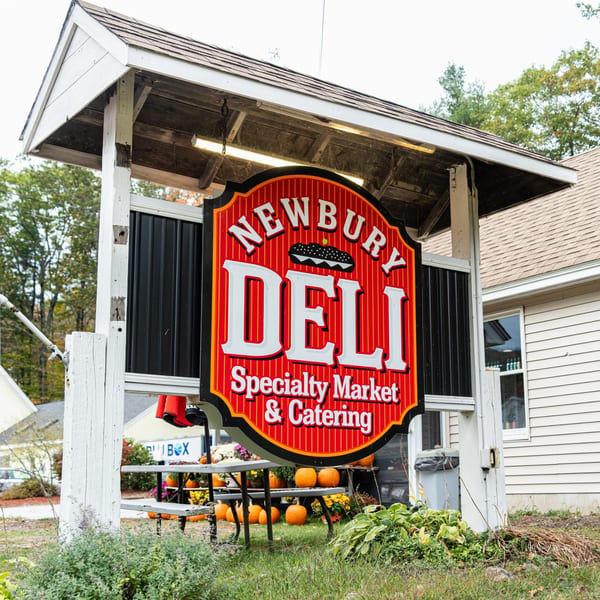 Newbury Deli sign, red and white, with pumpkins and fall decor outside the deli building.