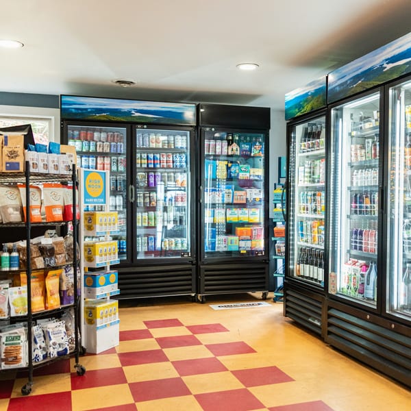 Interior of Newbury Deli with multiple refrigerators stocked with beverages and shelves of snacks.