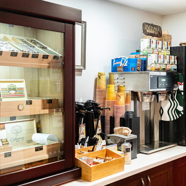A Newbury Deli counter with coffee, tea, cups, and a display case of cigars.