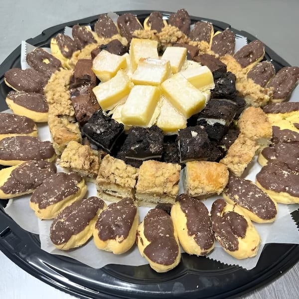 A black platter filled with assorted Newbury Deli pastries, including chocolate-dipped eclairs, brownies, and lemon bars.